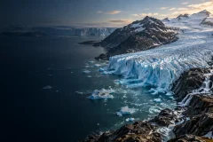 Blue glacier descending between dark mountain ridges under a warming sky
